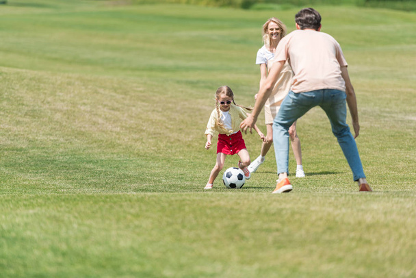 gelukkig gezin met een kind spelen met voetbal in park - Foto, afbeelding