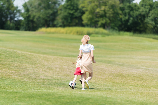 vista trasera de la madre y la pequeña hija jugando con la pelota de fútbol en el parque
 - Foto, Imagen