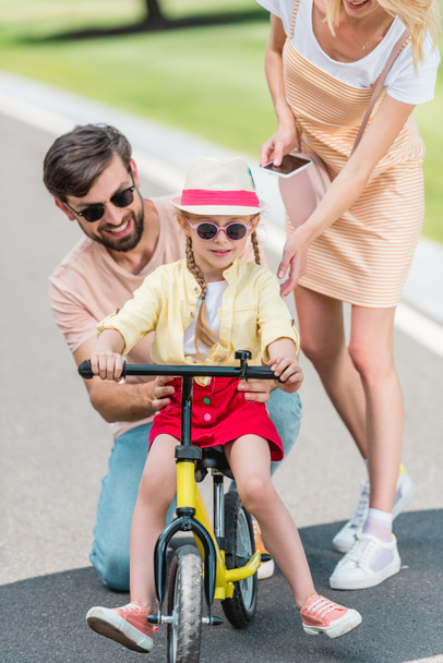 happy parents teaching little daughter riding bicycle in park - Fotografie, Obrázek