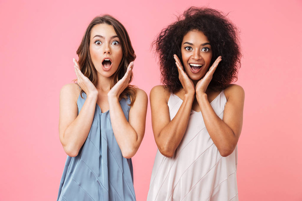 Two excited young girls dressed in summer clothes looking at camera and screaming isolated over pink background - Photo, image
