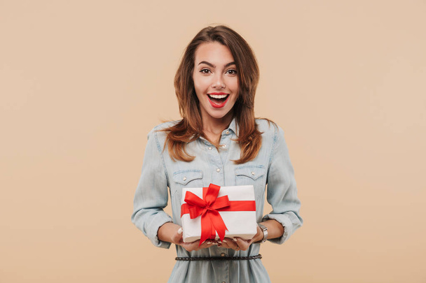 Portrait of an excited young girl holding present box isolated over beige background - Photo, Image