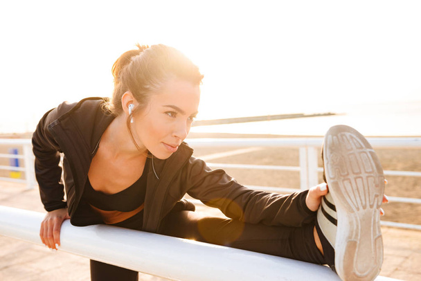 Image of young sports woman make stretching exercises outdoors on the street listening music. - Photo, Image