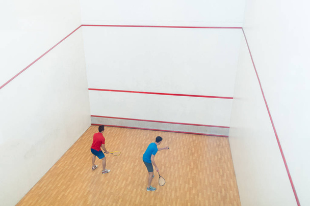 Takana näkymä kaksi kilpailukykyistä nuorta miestä pelaa squash peli
 - Valokuva, kuva