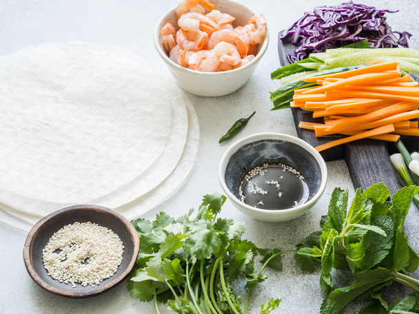 Ingredientes para cocinar rollos de primavera: zanahorias, pepinos, hierbas, col roja, camarones, papel de arroz sobre un fondo gris. Set de alimentos para cocinar rollos de primavera vietnamitas
. - Foto, imagen