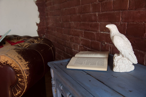 Figurine of an eagle with an open book and an old armchair against a brick wall background - Fotografie, Obrázek