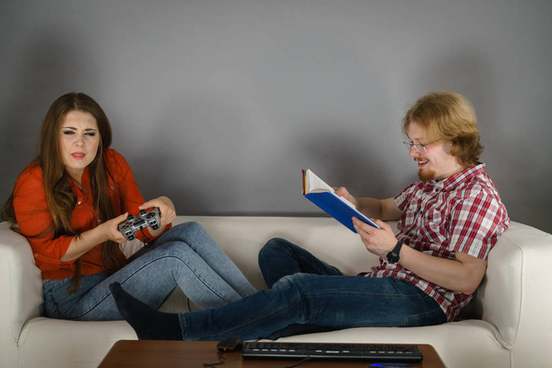 Kanepede oturan çift boş zaman geçiriyor. Kadın video oyunları oynuyor ve erkek kitap okuyor.. - Fotoğraf, Görsel