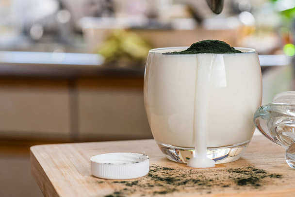 Lähikuva näkymä tuore kefir probiotik juoma kirkas lasi sekoittaa vihreä spirulina jauhe keittiön pöydälle
. - Valokuva, kuva