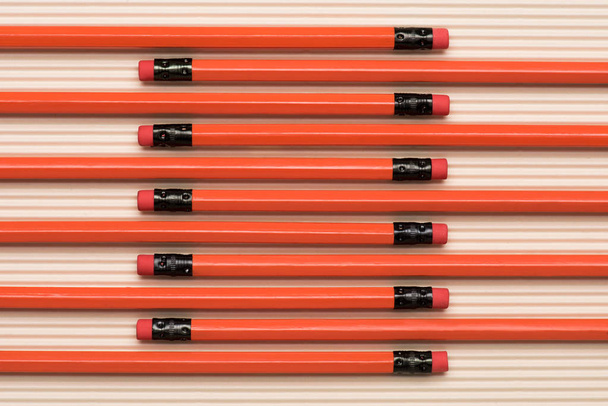 вид сверху на красные графитовые карандаши с ластиками, расположенными в ряд на бежевом
  - Фото, изображение