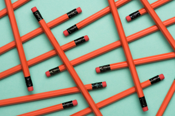 bovenaanzicht van gearrangeerde rode grafiet potloden met gummen op groen - Foto, afbeelding