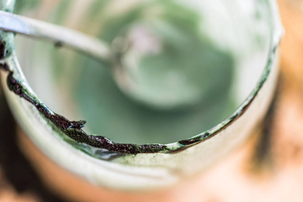 Overhead closeup view emptied glass with spoon of fresh kefir probiotik drink mixed with green spirulina powder on kitchen table - Photo, Image