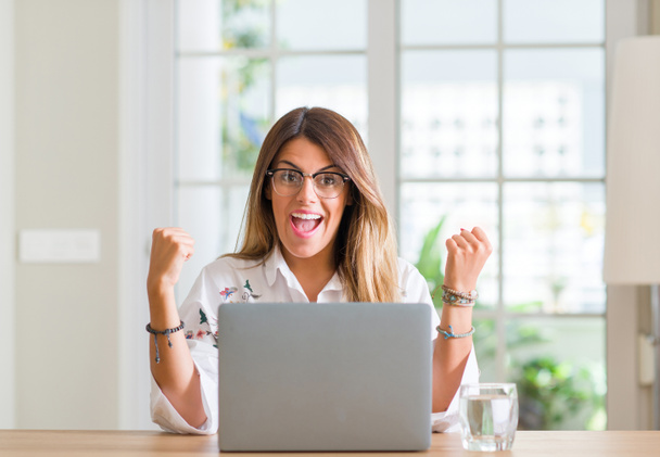 Nuori nainen kotona kannettavan tietokoneen avulla huutaa ylpeä ja juhlii voittoa ja menestystä hyvin innoissaan, hurraavat tunteita
 - Valokuva, kuva