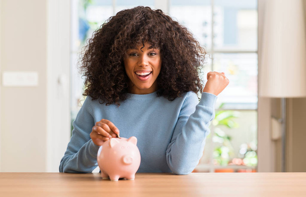 Afrikkalainen amerikkalainen nainen säästää rahaa säästöpossu huutaa ylpeä ja juhlii voittoa ja menestystä hyvin innoissaan, hurraavat tunteet
 - Valokuva, kuva