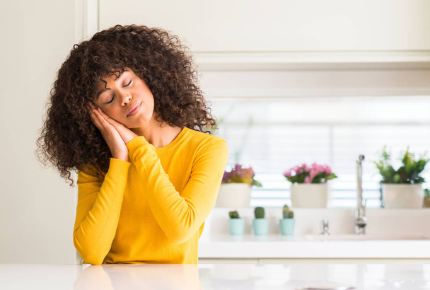 afrikanisch-amerikanische Frau trägt gelben Pullover in der Küche schlafen müde träumend und posiert mit den Händen zusammen, während sie mit geschlossenen Augen lächelt. - Foto, Bild
