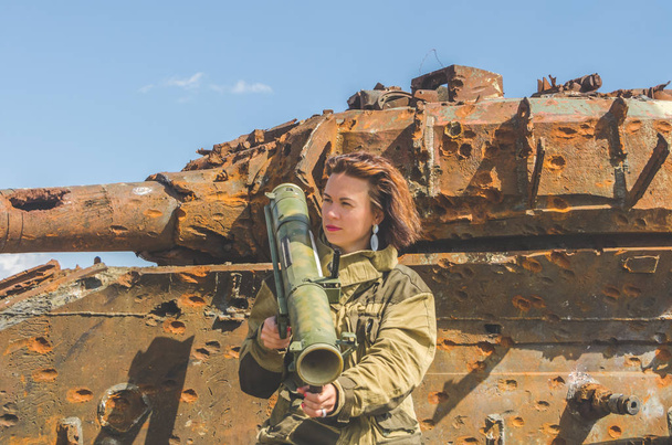 Sunny day girl in uniform with a Bazooka on the background of a broken tank on the battlefield - Foto, Bild
