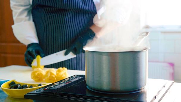 Close-up of a steaming saucepan on a stove when chef cleans a lemon - Фото, изображение