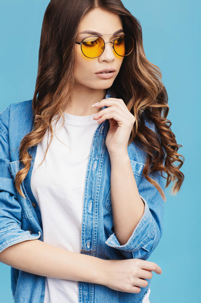 Portrait of a beautiful young girl in sunglasses on a blue background. - Fotó, kép