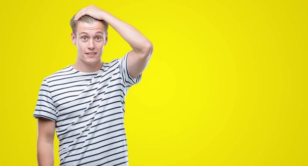 Young handsome blond man wearing stripes sailor t-shirt stressed with hand on head, shocked with shame and surprise face, angry and frustrated. Fear and upset for mistake. - 写真・画像
