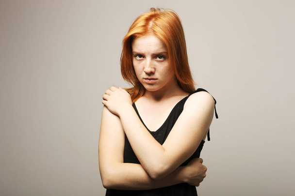 Beautiful fragile redheaded young woman in the dark. Sad frightened girl scared of abuse. Nonverbal behavior, body language. Red hair female looking stressed out & depressed. Background, close up. - Fotoğraf, Görsel