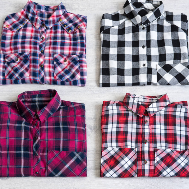 Four multi-colored checkered women's shirts lying neatly folded on a light wooden background - Фото, зображення