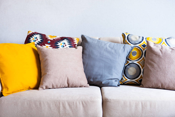 Multi-colored pillows on a beige fabric sofa, the concept of home comfort and cozy, copy space, close-up - Foto, Bild