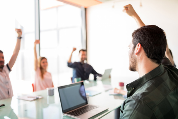 Uomo che alza la mano con i colleghi in sala riunioni, team aziendale che mostra positività
  - Foto, immagini