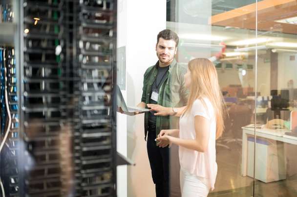 Two business people standing in server room with laptop and discussing - Photo, Image