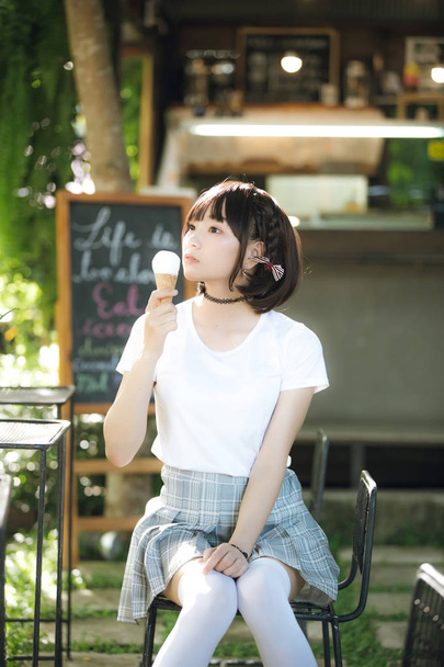 portrait of asian girl with white shirt and skirt eating ice cream in outdoor nature vintage film style - Fotó, kép