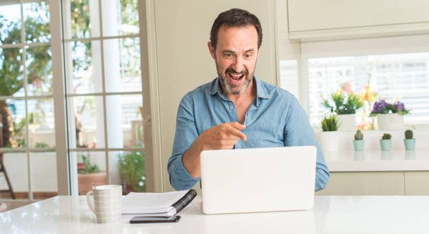 Middle age man using laptop at home very happy pointing with hand and finger - Foto, Bild