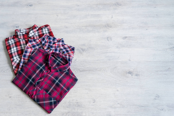 Three multi-colored checkered women's shirts lying neatly folded on a light wooden background - Foto, Bild