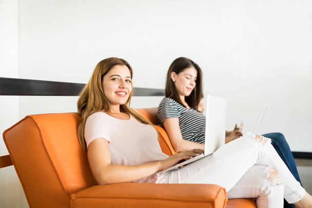 Muotokuva kaunis nuori latino nainen laptop istuu sohvalla kollegansa takana
  - Valokuva, kuva