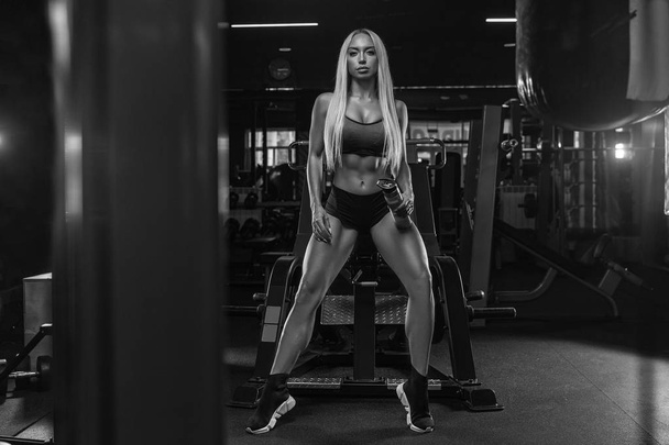 beautiful girl bodybuilder , execute exercise with dumbbells, in dark gym - Fotó, kép