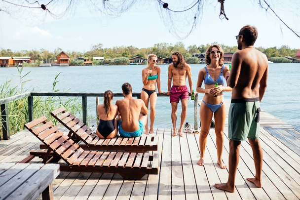 Group of young people in swimwear standing on deck and enjoying summertime vacation together. - Foto, Bild