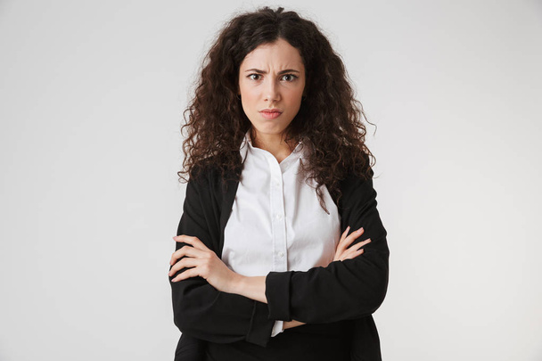 Portrait of an upset young businesswoman standing with arms folded and looking at camera isolated over white background - Fotoğraf, Görsel