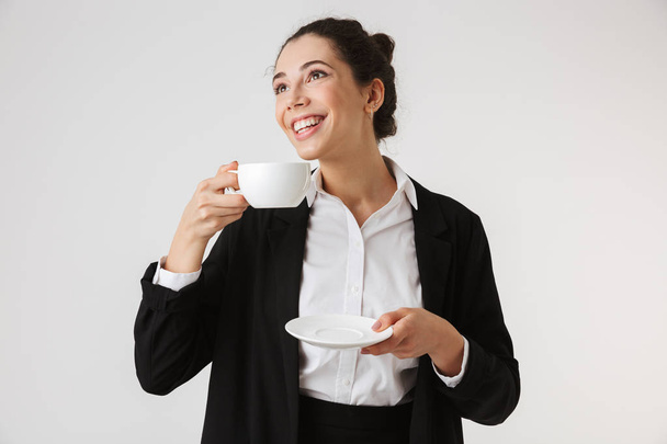 Portrait of a smiling young businesswoman drinking tea from a cup isolated over white background - Zdjęcie, obraz