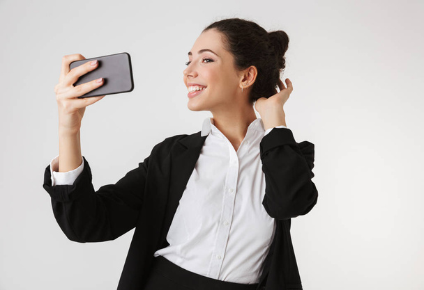Portrait of a pretty young businesswoman taking a selfie isolated over white background - Foto, Bild