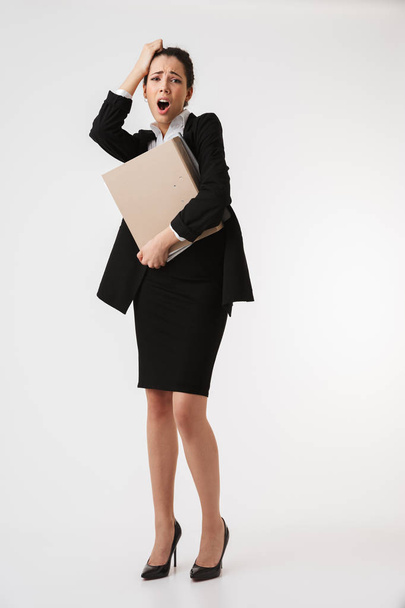 Full length portrait of an exhausted young businesswoman holding folders isolated over white background - Foto, Imagem