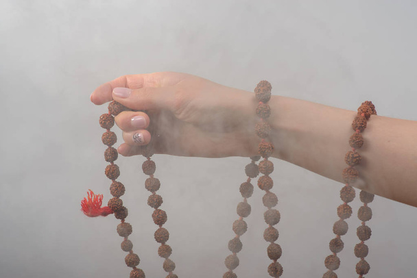 Female hand with rosary on a gray background in smoke - Fotografie, Obrázek