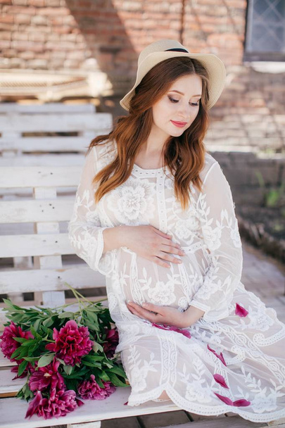 Hermosa mujer embarazada en vestido blanco y sombrero de paja con flores
 - Foto, imagen