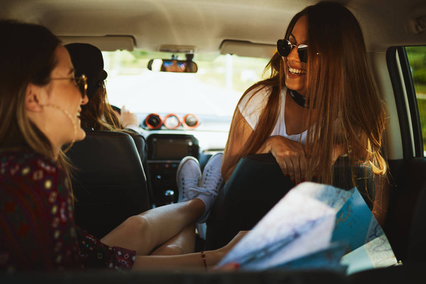 Drie jonge vrouwen kijken naar kaart en plezier op roadtrip. - Foto, afbeelding