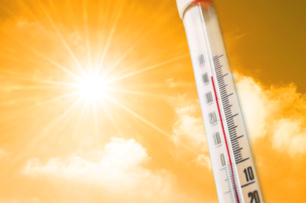 Thermometer tegen de achtergrond van een oranje geel warme gloed van wolken en zon, concept van warm weer - Foto, afbeelding