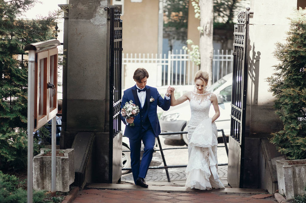 stylish groom and bride walking and holding hands in city street, hugging and embracing. wedding day concept. beautiful wedding couple, romantic moments elopment - Photo, Image