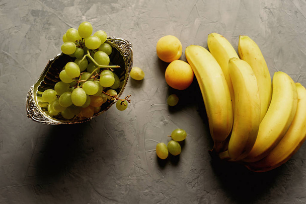 Свіжі та соковиті фрукти, банани, персики, виноград на сірому фоні. Здорове харчування
 - Фото, зображення