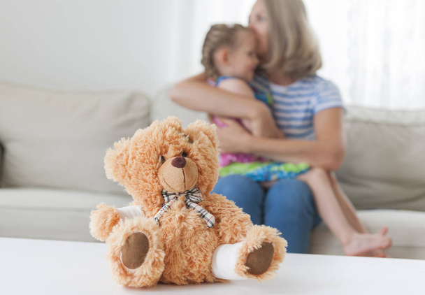 ein Teddybär mit einer Pfote. Mutter küsst ihre Tochter im Hintergrund - Foto, Bild