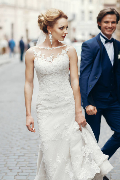 stylish bride walking and groom running after her in city street. happy luxury wedding couple having fun and dancing . romantic  moment. - Photo, Image