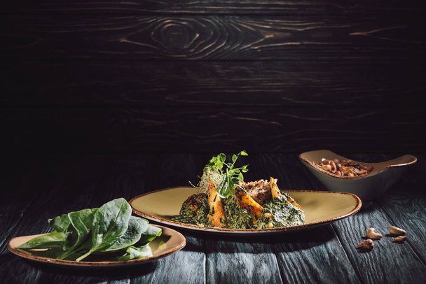 piatti con foglie di spinaci e panikesh vicino ciotola con anacardi sul tavolo di legno
  - Foto, immagini