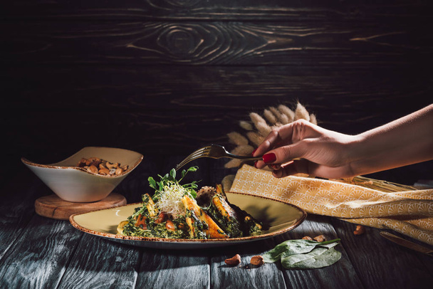 abgeschnittenes Bild einer Frau, die Panikesch mit Cashewnüssen und Spinat mit der Gabel über den Tisch isst  - Foto, Bild
