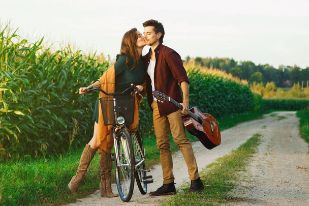 junges Paar zu Fuß auf Landstraße. Mädchen fährt Fahrrad und Kerl hält Gitarre. - Foto, Bild