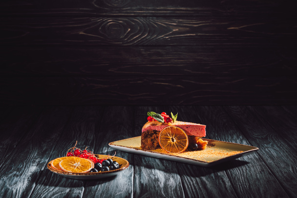 porkkanakakku marjatäytteellä ja appelsiiniviipaleilla, mustikoilla ja karpaloilla lautasella
  - Valokuva, kuva