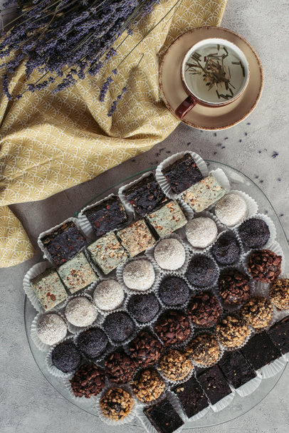 επίπεδη lay με φλιτζάνι τσάι από βότανα, γλυκά επιδόρπια και λεβάντας σε τραπεζομάντιλο σε γκρι επιτραπέζια - Φωτογραφία, εικόνα