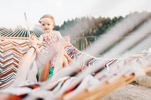 щаслива стильна сім'я, що грає з милою дочкою, відпочиває в гамаку на літніх канікулах у вечірньому сонячному світлі на пляжі. Хіпстерська пара з дитиною відпочиває і розважається під час заходу сонця. простір для тексту
 - Фото, зображення
